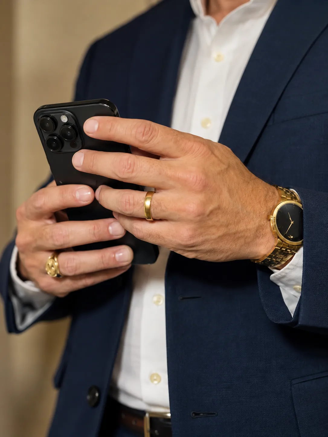 A man in a navy suit holding a phone in both hands.